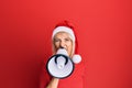 Young blonde woman wearing christmas hat screaming using megaphone over isolated red background Royalty Free Stock Photo