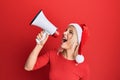 Young blonde woman wearing christmas hat screaming using megaphone over isolated red background Royalty Free Stock Photo