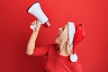 Young blonde woman wearing christmas hat screaming using megaphone over isolated red background Royalty Free Stock Photo