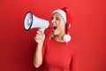 Young blonde woman wearing christmas hat screaming using megaphone over isolated red background Royalty Free Stock Photo