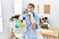 Young blonde woman wearing cleaner uniform holding cleaning products thinking worried about a question, concerned and nervous with