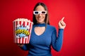 Young blonde woman wearing 3d glasses and eating pack of popcorn watching a movie on cinema with a big smile on face, pointing Royalty Free Stock Photo