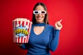 Young blonde woman wearing 3d glasses and eating pack of popcorn watching a movie on cinema cheerful with a smile on face pointing Royalty Free Stock Photo