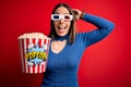 Young blonde woman wearing 3d glasses and eating pack of popcorn watching a movie on cinema Crazy and scared with hands on head, Royalty Free Stock Photo