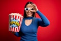 Young blonde woman wearing 3d glasses and eating pack of popcorn watching a movie on cinema doing ok gesture with hand smiling, Royalty Free Stock Photo