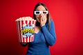 Young blonde woman wearing 3d glasses and eating pack of popcorn watching a movie on cinema laughing and embarrassed giggle Royalty Free Stock Photo