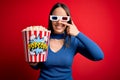 Young blonde woman wearing 3d glasses and eating pack of popcorn watching a movie on cinema Pointing with hand finger to face and Royalty Free Stock Photo