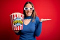 Young blonde woman wearing 3d glasses and eating pack of popcorn watching a movie on cinema smiling cheerful presenting and Royalty Free Stock Photo