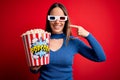 Young blonde woman wearing 3d glasses and eating pack of popcorn watching a movie on cinema smiling cheerful showing and pointing Royalty Free Stock Photo