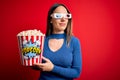 Young blonde woman wearing 3d glasses and eating pack of popcorn watching a movie on cinema smiling looking to the side and Royalty Free Stock Photo