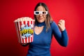 Young blonde woman wearing 3d glasses and eating pack of popcorn watching a movie on cinema very happy and excited doing winner Royalty Free Stock Photo