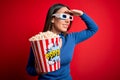 Young blonde woman wearing 3d glasses and eating pack of popcorn watching a movie on cinema very happy and smiling looking far Royalty Free Stock Photo