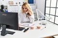 Young blonde woman wearing dentist uniform speaking on the phone at dental clinic