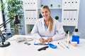 Young blonde woman wearing dentist uniform writing on clipboard at clinic