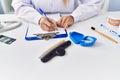 Young blonde woman wearing dentist uniform writing on clipboard at clinic