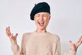 Young blonde woman wearing french look with beret crazy and mad shouting and yelling with aggressive expression and arms raised Royalty Free Stock Photo