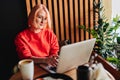 Young blonde woman wearing red casual sweater in cafe working on the laptop computer and drinking coffe Royalty Free Stock Photo