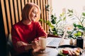 Young blonde woman wearing red casual sweater in cafe working on the laptop computer and drinking coffe Royalty Free Stock Photo