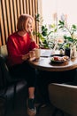 Young blonde woman wearing red casual sweater in cafe working on the laptop computer and drinking coffe Royalty Free Stock Photo