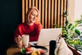 Young blonde woman wearing red casual sweater in cafe working on the laptop computer and drinking coffe Royalty Free Stock Photo