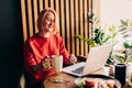 Young blonde woman wearing red casual sweater in cafe working on the laptop computer and drinking coffe Royalty Free Stock Photo