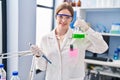 Young blonde woman wearing scientist uniform measuring liquid on test tube at laboratory Royalty Free Stock Photo