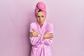 Young blonde woman wearing shower towel cap and bathrobe shaking and freezing for winter cold with sad and shock expression on Royalty Free Stock Photo