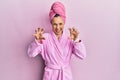 Young blonde woman wearing shower towel cap and bathrobe smiling funny doing claw gesture as cat, aggressive and sexy expression Royalty Free Stock Photo