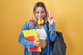 Young blonde woman wearing student backpack and holding books gesturing finger crossed smiling with hope and eyes closed Royalty Free Stock Photo