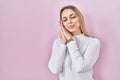Young blonde woman wearing white sweater over pink background sleeping tired dreaming and posing with hands together while smiling Royalty Free Stock Photo