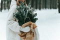Blonde woman wears white fur coat and knitted hat posing with fir tree in winter forest. Winter fashion Royalty Free Stock Photo