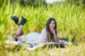 Young blonde woman in white dress lies on a picnic sheet in tall grass Royalty Free Stock Photo