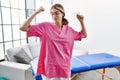 Young blonde woman working as physiotherapist at home showing arms muscles smiling proud Royalty Free Stock Photo