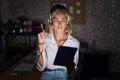 Young blonde woman working at the office at night pointing up looking sad and upset, indicating direction with fingers, unhappy Royalty Free Stock Photo