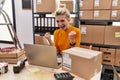 Young blonde woman working at small business ecommerce using laptop screaming proud, celebrating victory and success very excited Royalty Free Stock Photo