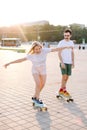 Young blondhaired woman longboarding with her partner, boths are in the bright shorts of pink
