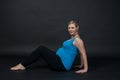 Young blondy pregnant woman in blue tank top does exercises, black background.