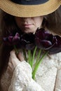 Young bohemian woman in vintage retro cloth and a hat smelling bouquet of purple tulips