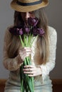 Young bohemian woman in vintage retro cloth and a hat smelling bouquet of purple tulips