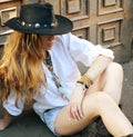 Young boho style woman have a rest sitting on a town street against old door, hippie, indie style