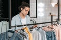 Young boutique owner choosing shirts on hangers and smiling