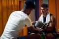 Young boxing player with coach in gym dressing room sitting on bench