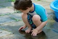 young boy in a bathing suit playing in a puddle of water in the backyard next to a shallow swimming pool