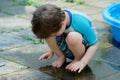 young boy in a bathing suit playing in a puddle of water in the backyard next to a shallow swimming pool Royalty Free Stock Photo