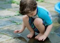 young boy in a bathing suit playing in a puddle of water in the backyard next to a shallow swimming pool