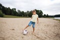 A young boy on the beach runs towards a soccer ball and wants to score a goal on a warm summer day