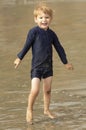 Young boy with blonde hair and navy swimsuit having fun splashing at the beach