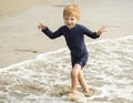 Young boy with blonde hair and navy swimsuit having fun splashing at the beach Royalty Free Stock Photo