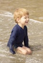 Young boy with blonde hair and navy swimsuit having fun splashing at the beach Royalty Free Stock Photo