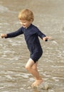 Young boy with blonde hair and navy swimsuit having fun splashing at the beach Royalty Free Stock Photo